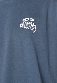 Blue cotton t-shirt featuring a white graphic design with stylized text "KARMA" and abstract elements on the left side.