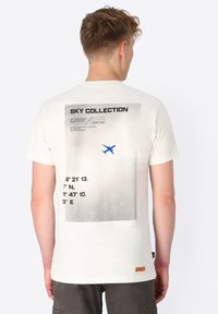 Cream-colored T-shirt with a graphic print featuring coordinates and an airplane silhouette in blue, displayed on the back. Cotton fabric.