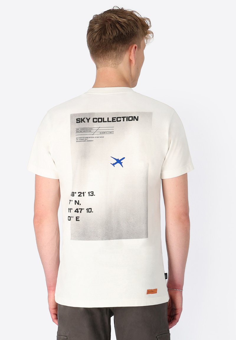 Cream-colored T-shirt with a graphic print featuring coordinates and an airplane silhouette in blue, displayed on the back. Cotton fabric.