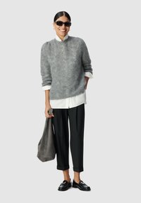 Grijze gebreide trui met een hoge kraag, een witte overhemd eronder, zwarte broek, zwarte schoenen en een grijze suède tas. Zonnebril inbegrepen.