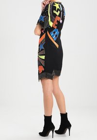 Svart kort klänning med färgglada pärlade bokstäver och stjärnmönster. Accentuerad med en vågig nederkant och i kombination med svarta ankelstövlar.