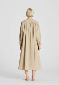 Robe en coton beige clair, à manches longues, longueur cheville avec une coupe décontractée, dotée d'une fermeture à boutons et de détails froncés à l'arrière.
