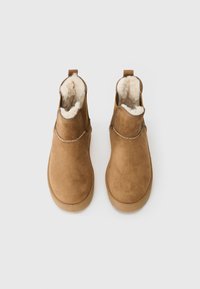Pair of brown suede slip-on boots with plush white fur lining, viewed from above on a white background.