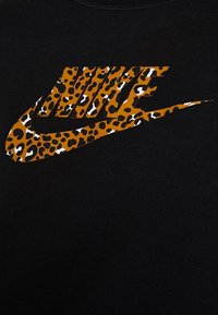 Svart sweatshirt med en framträdande, texturerad leopardtryck av Nike-logotypen i varma toner av orange och brunt, mot en mörk bakgrund.