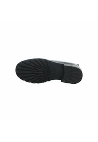 Schwarze Schuhsohle mit tiefem Profil und kreisförmigem Logodetail in der Mitte, fotografiert vor einem weißen Hintergrund.