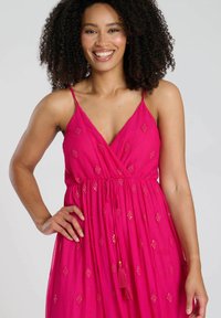 Rosa, ärmelloses Kleid mit V-Ausschnitt, das mit gestickten Mustern und einem Bindeband in der Taille versehen ist. Leichter Stoff mit einer sanften Textur.