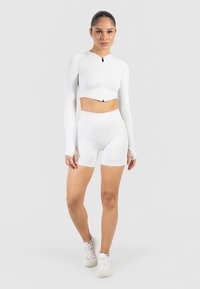 White cropped zip-up long-sleeve top paired with high-waisted shorts, made of smooth fabric, featuring a sleek, seamless design.