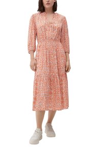 Pomarańczowa kwiatowa sukienka midi z dekoltem w serek, rękawami 3/4, elastyczną talią i warstwową spódnicą. Noszona z białymi trampkami.