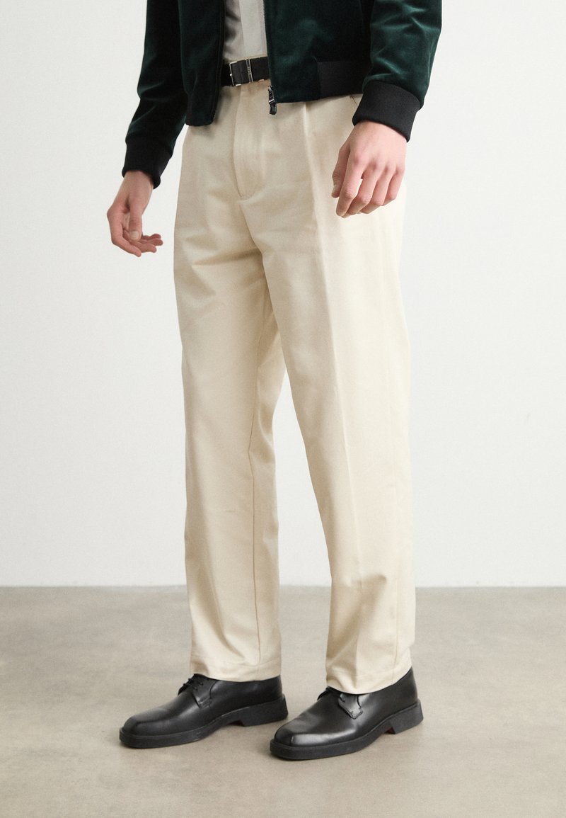 Cream-colored, wide-leg trousers with a smooth texture, paired with black leather shoes. The outfit features a dark green bomber jacket.
