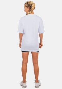 Witte oversized t-shirt met korte mouwen, gladde textuur, ronde halslijn. Draag het met zwarte shorts en grijze sportschoenen.