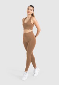 Bruine geribbelde sportbeha en bijpassende high-waisted leggings, beiden gemaakt van rekbaar materiaal, gecombineerd met witte sportschoenen.