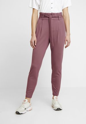 Pantalons mauves étirables et fuselés avec une taille haute ceinturée et des poches latérales, associés à des baskets blanches. Tissu lisse avec une finition élégante.