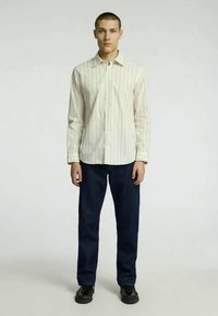 Valge triibuline noolekraega särk pikkade varrukatega, kombineeritud tumepruunide pükste ja mustade kingadega. Sile kangas, klassikaline lõige, struktureeritud krae.