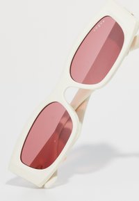 Hvite innfattede rektangulære solbriller med rosa tonede glass vinklet mot en lys bakgrunn, med ordet "vogue" på ett glass.