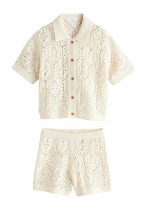 Krém színű kötött rövid ujjú gombos felső és hozzáillő, magas derekú kötött rövidnadrág nyitott geometriai mintákkal.