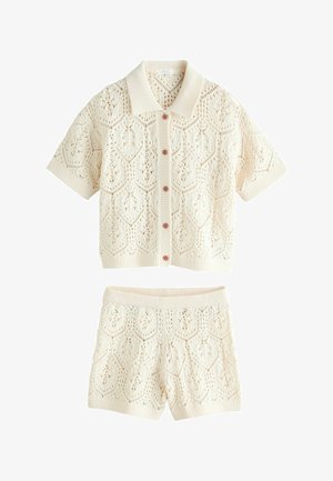 Krémový pletený krátky rukáv na gombíky a zodpovedajúce pletené šortky s vysokým pásom s otvorenými geometrickými vzormi.
