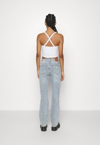 Witte cropped tanktop met kruisende banden, gecombineerd met lichtblauwe flared jeans. Gestructureerd denim met een leren merketiket op de achterkant.