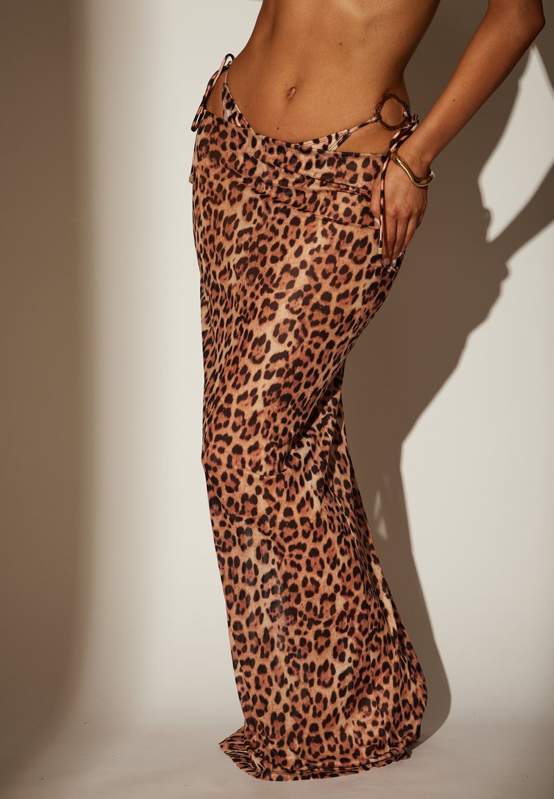 Falda maxi de estampado de leopardo, confeccionada con tela ligera. Presenta lazos laterales y una silueta fluida. La paleta de colores incluye tonos beige y manchas marrón oscuro.