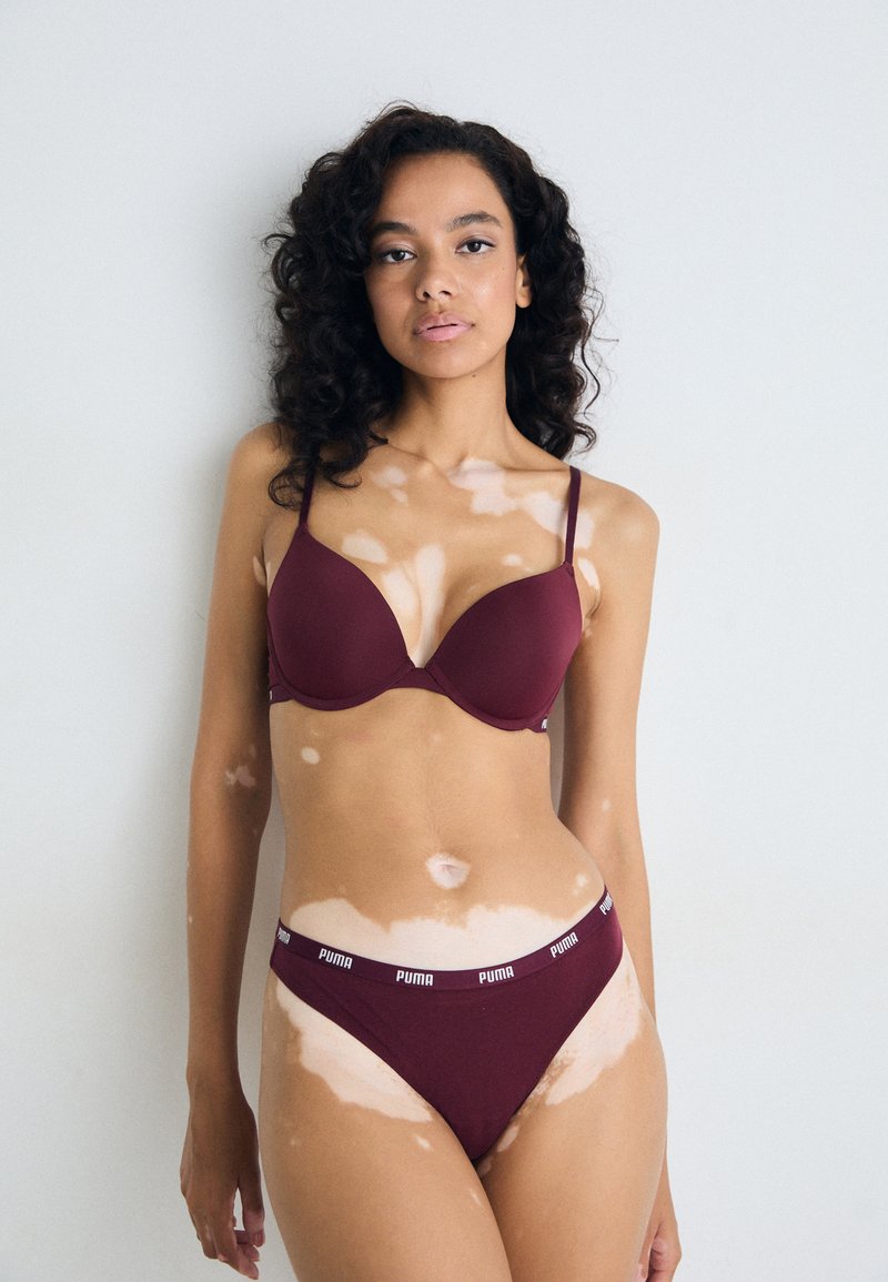 Bordeaux bh met gevormde cups en verstelbare bandjes, gecombineerd met bijpassende bikini slipjes met een merkband, gladde textuur.