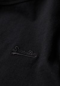Czarny bawełniany t-shirt o miękkiej fakturze, z haftowanym logo "SuperDry" w dopasowanej czarnej nici, umiejscowionym blisko dołu.