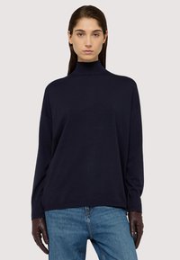 Maglione a collo alto di colore blu navy con maniche lunghe, morbido al tatto e con vestibilità morbida, abbinato a jeans in denim e guanti marroni.