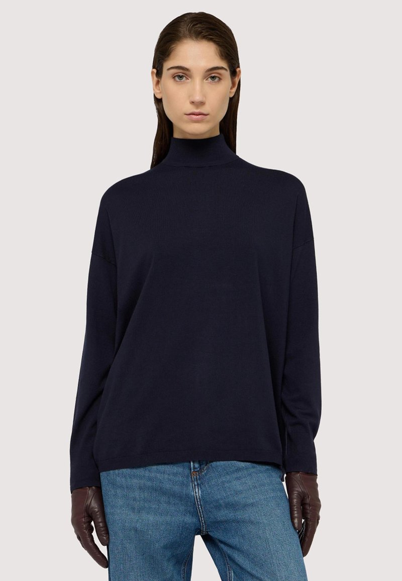 Maglione a collo alto di colore blu navy con maniche lunghe, morbido al tatto e con vestibilità morbida, abbinato a jeans in denim e guanti marroni.