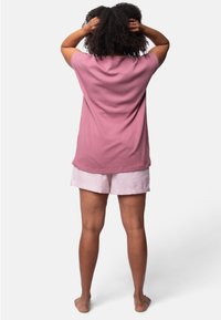 Top a maniche corte rosa chiaro con una finitura testurizzata, abbinato a pantaloni corti a righe bianche e rosa. Design semplice, vestibilità rilassata.