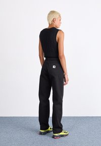 Black knit sleeveless top and high-waisted black denim jeans. Model wears bright green and black athletic sneakers. Flat, light gray background.