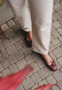 Burgundy nahkakengät ballerinat pyöreällä kärjellä, joissa on koristeellinen nauha ja sileä pinta, käytettynä vaaleaväristen, leveälahkeisten housujen kanssa.