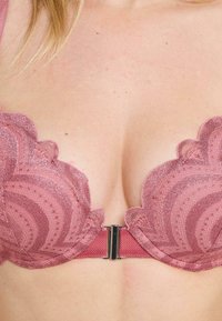 Soutien-gorge rose avec détails en dentelle festonnée, présentant un motif texturé et une fermeture métallique à l'arrière.