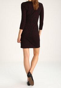 Czarna sukienka z teksturowanym kwiatowym wzorem, z rękawami o długości trzy czwarte i dopasowanym krojem. Noszona z czarnymi balerinami, prezentującymi gładkie wykończenie.