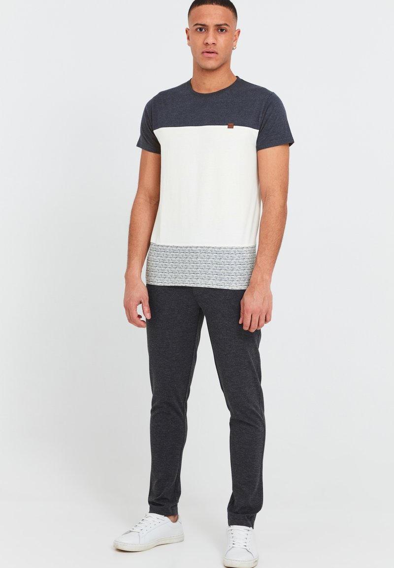 T-shirt med korte ærmer i en hvid og marineblå farveblokdesign, tekstureret grå bundbånd, suppleret med mørke bukser og hvide sneakers.