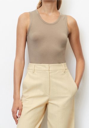 Beige ærmeløs top lavet af blødt stof med rund halsudskæring, parret med højhalsede, lys gule bredbenede bukser med lommer.