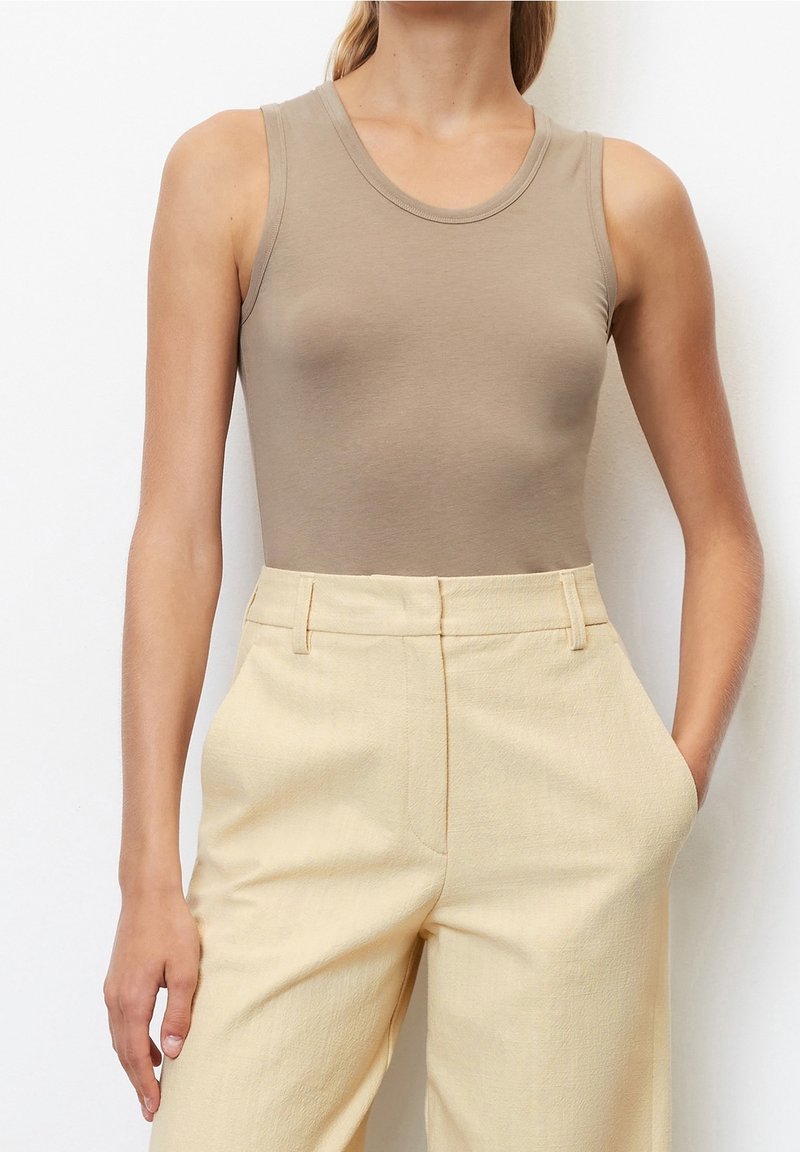 Top sin mangas color beige, hecho de una tela suave con un escote redondo, combinado con pantalones de pierna ancha de talle alto en un suave color amarillo claro que cuentan con bolsillos.