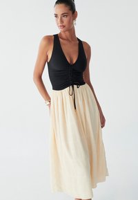 Black ribbed top with a deep v-neck and gathered detail, paired with a flowy, cream-colored midi skirt featuring a textured pattern.