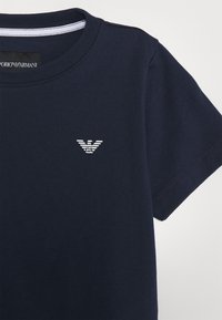 Marinblå bomullströja med rund halsringning och korta ärmar. Har en vit broderad logotyp på vänster bröst. Slät textur.