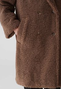 Brauner, strukturierter, doppelt geknöpfter Mantel mit einer weichen, flauschigen Oberfläche, ausgestattet mit zwei Knöpfen und seitlichen Taschen.
