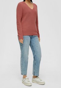 Rostfarbener Langarm-V-Ausschnitt-Pullover mit gerippter Textur, kombiniert mit hellblauen geraden Jeans und weißen Sneakern.