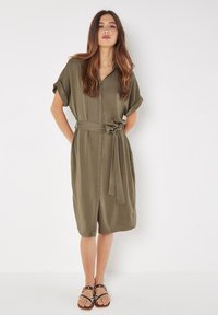 Olivengrünes Hemdkleid mit kurzen umgeschlagenen Ärmeln, Gürtel in der Taille und durchgehender Knopfleiste. Glatter Stoff mit lässiger Passform.