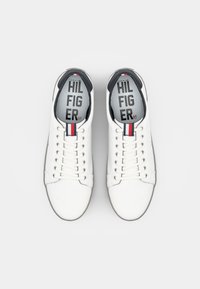 Witte leren sneakers met een ronde neus, contrasterende marineblauwe accenten, en een rood-wit-blauwe streep op de tong. Veters en logo zichtbaar.