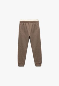 Braune, strukturierte Jogginghosen mit zulaufendem Bein, elastischem Bund und cremefarbener Innenseite am Bund. Keine Taschen oder Verzierungen.