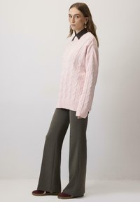 Pulover oversized de culoare roz deschis, tricotat cu aspect de cablu, cu manșete cu nervuri, asortat cu pantaloni largi de culoare verde măsliniu și pantofi cu accente burgundy.