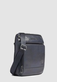 Borsa a tracolla in pelle blu con tracolla regolabile, tasca frontale con zip, logo impresso e texture liscia. Design compatto rettangolare.