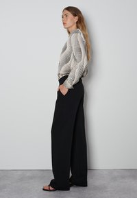 Blouse blanche avec des rayures horizontales noires, munie de manches bouffantes, associée à un pantalon large taille haute noir et des sandales plates.