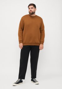 Bruine sweatshirt met een ronde hals, gecombineerd met zwarte tapered broek en marineblauwe sneakers. Smooth textuur, casual pasvorm.