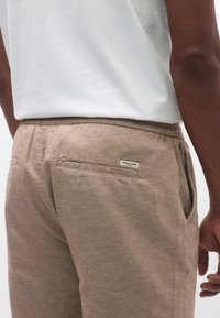 Μπεζ λινά παντελόνια με υφή, ελαστική μέση και δύο πίσω τσέπες. Η ετικέτα της μάρκας είναι ορατή στην δεξιά πίσω τσέπη.