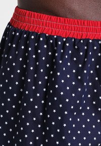 Gonna di tessuto blu navy con motivo di stelle bianche. Vita elastica rossa. Materiale leggero con una vestibilità morbida e texture liscia.
