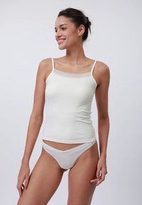 Top de alças branco canelado com alças finas, apresentando borda de renda em forma de escalope no decote. Combinado com fio dental a condizer com detalhes em renda.