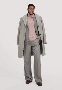 Grijze wollen jas over een roze coltrui en lichtgrijze op maat gemaakte broeken. De outfit heeft een losse pasvorm met een gestructureerde textuur.