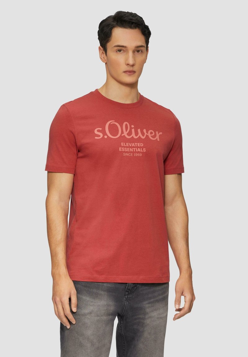 Rotes Baumwoll-T-Shirt mit Rundhalsausschnitt, das einen grafischen Druck in hellrosa Text zeigt, der "s.Oliver ELEVATED ESSENTIALS SINCE 1969" liest.